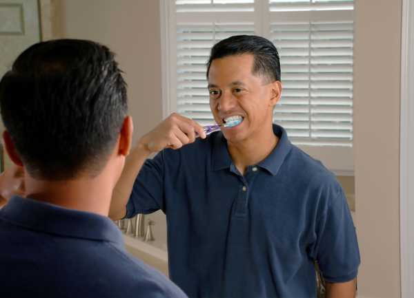 Man brushing his teeth in front of a bathroom mirror